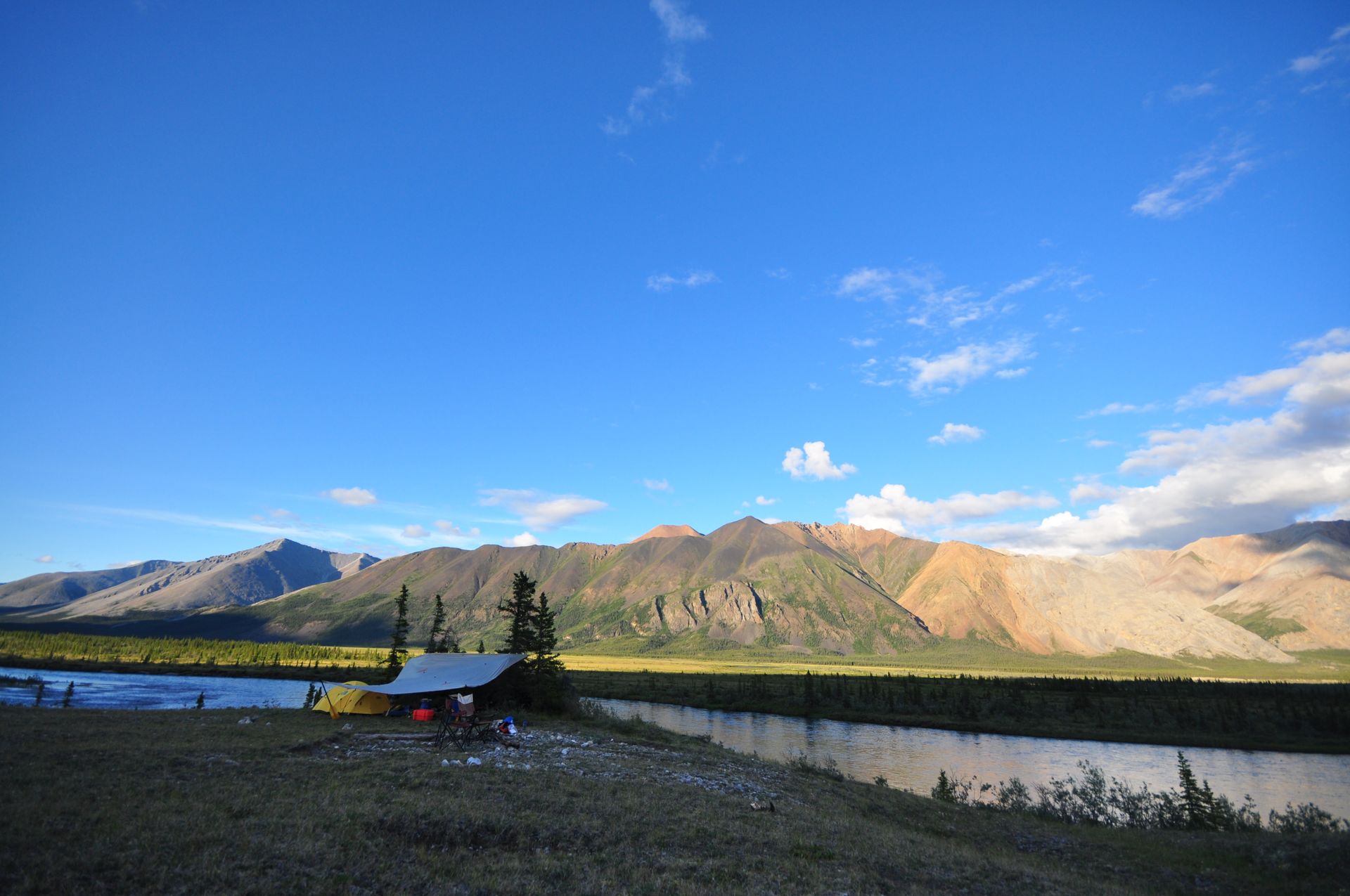 Mountain lake with blue sky, rocky peaks, and a small shoreline cabin under scattered clouds