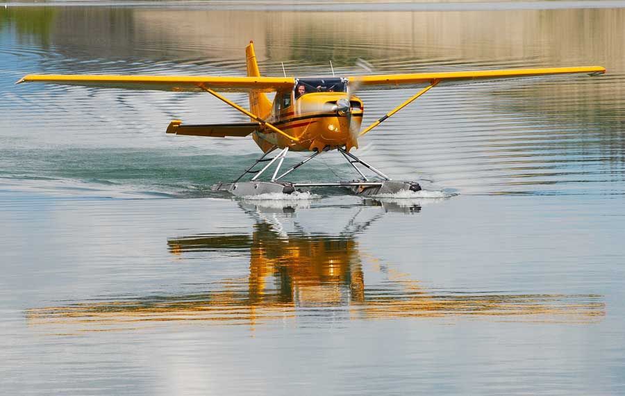 Yellow seaplane floating on calm water with its reflection visible