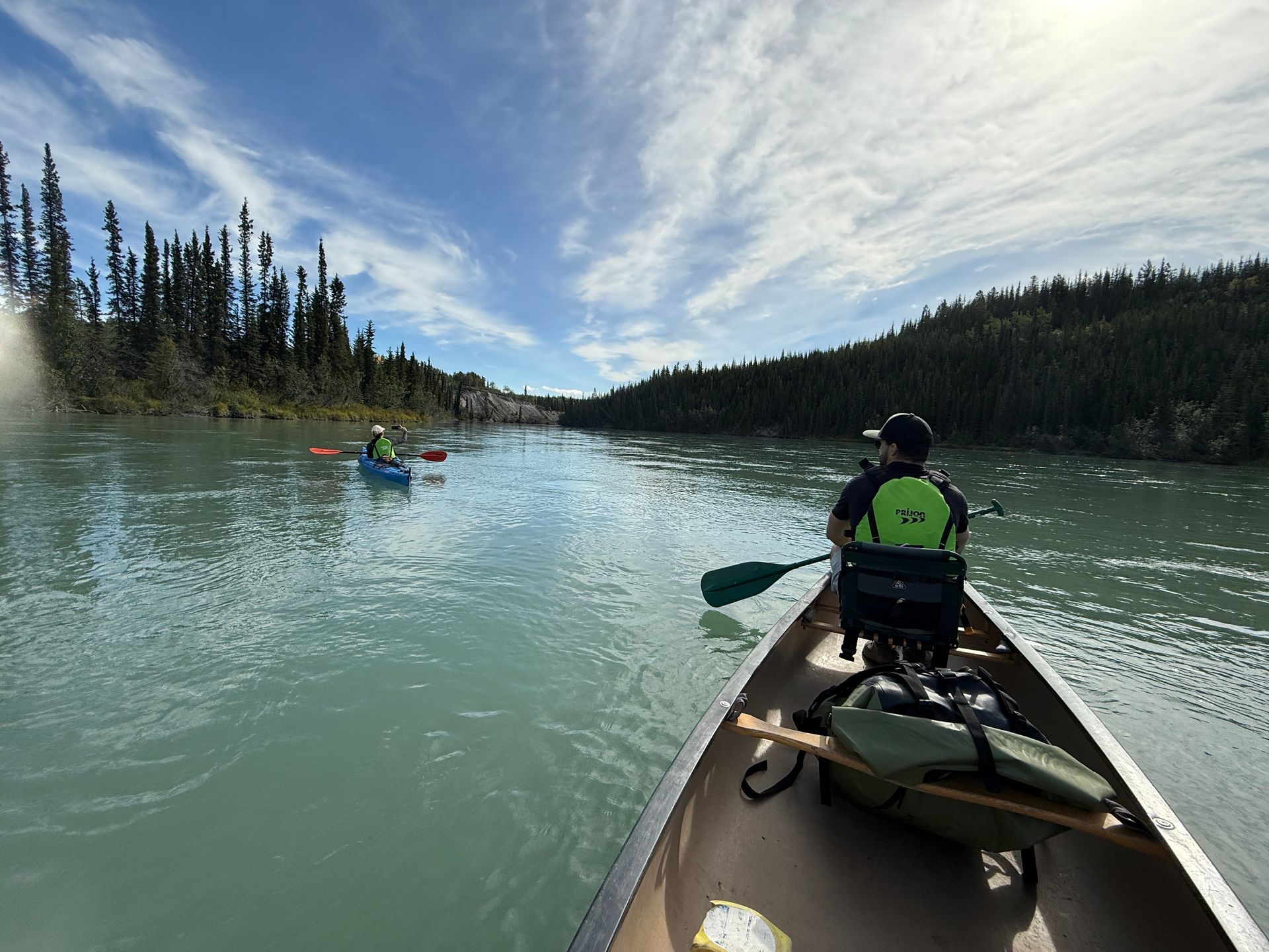 Kayak on a calm lake with paddlers ahead, surrounded by forested hills under a cloudy sky.