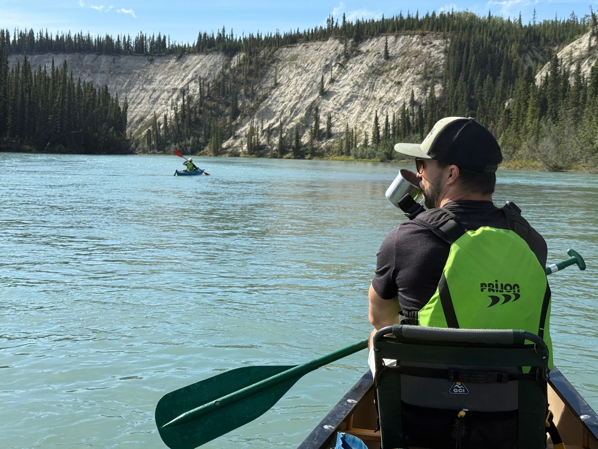 Two people in a green canoe on a blue lake, with forested cliffs in the background.