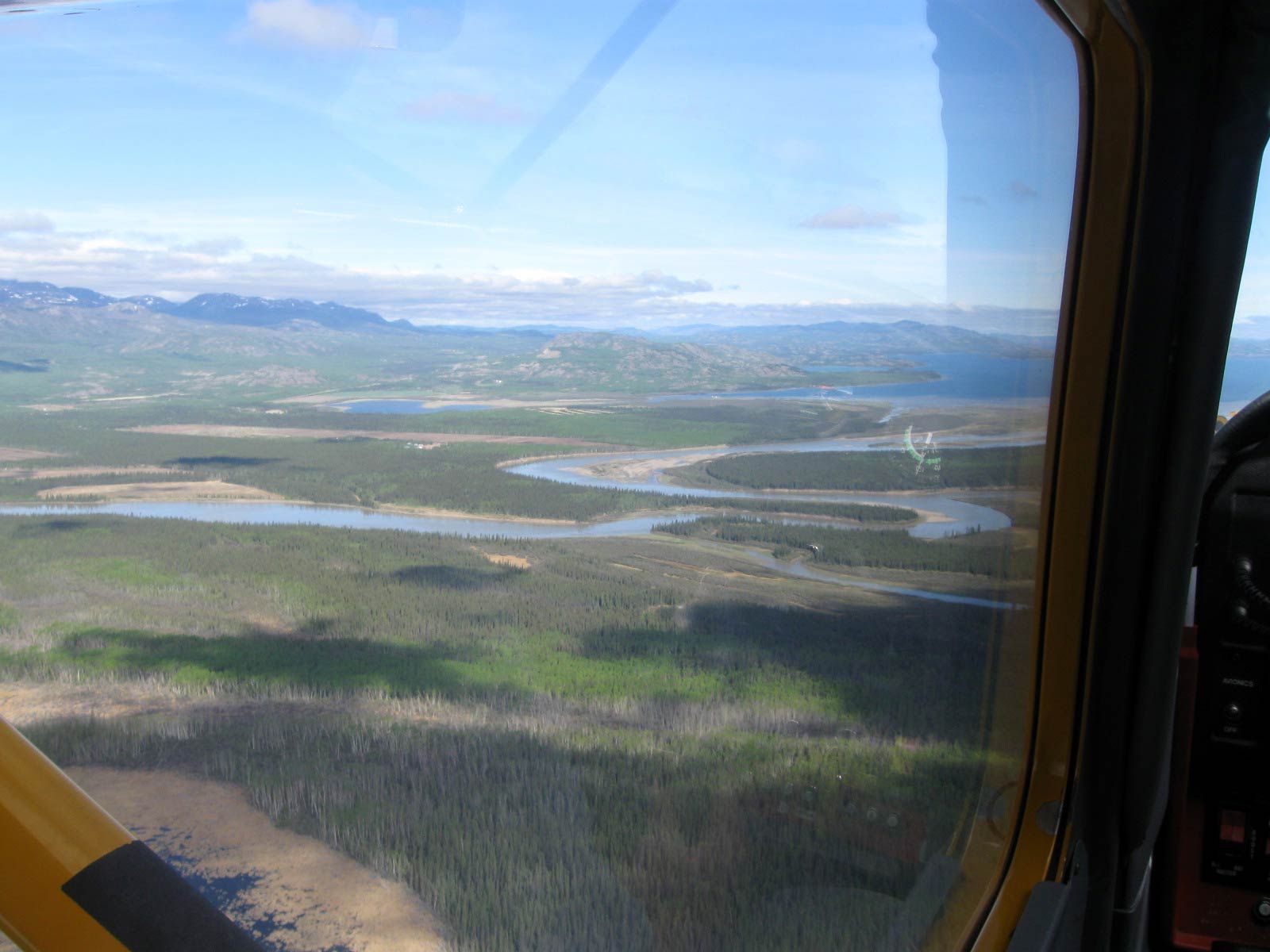 View from a vehicle window over wetlands, winding water, and distant mountains under a clear blue sky
