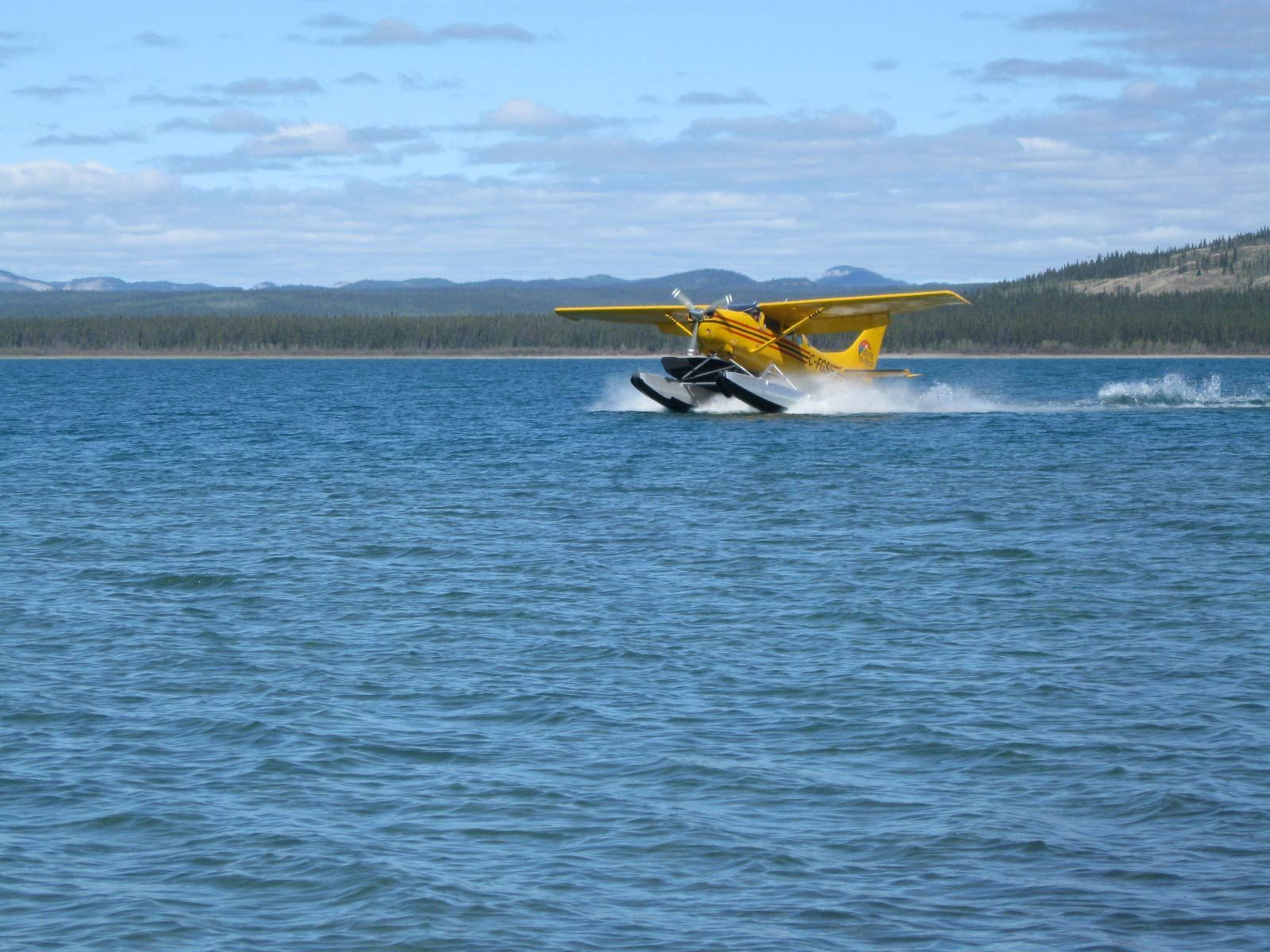 Yellow seaplane skimming across a blue lake with mountains in the distance