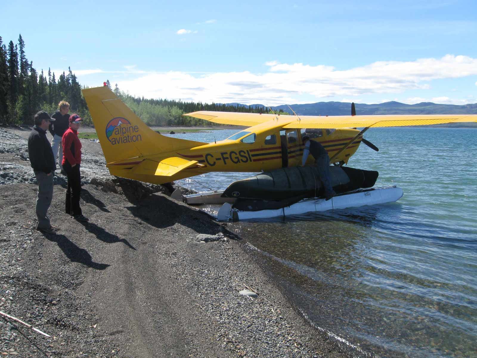 Yellow floatplane on a rocky lakeshore with two people standing nearby under a clear sky