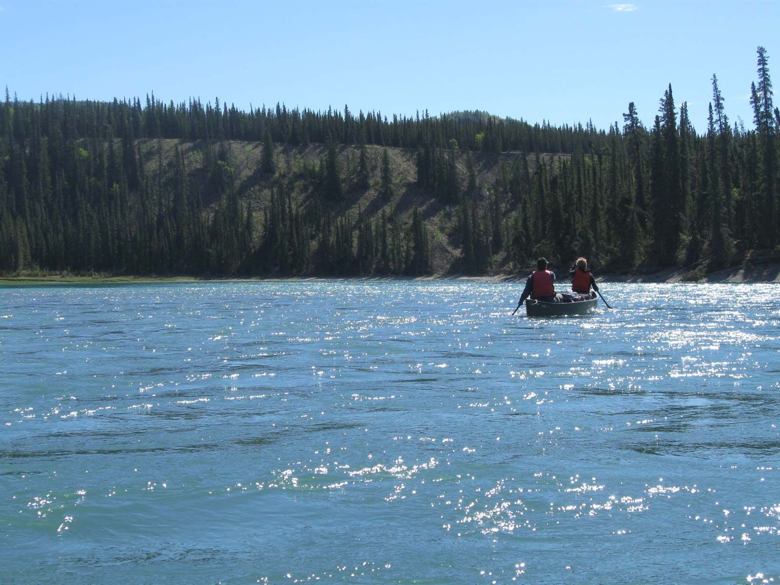Two people canoeing on a sparkling blue lake with forested cliffs in the background