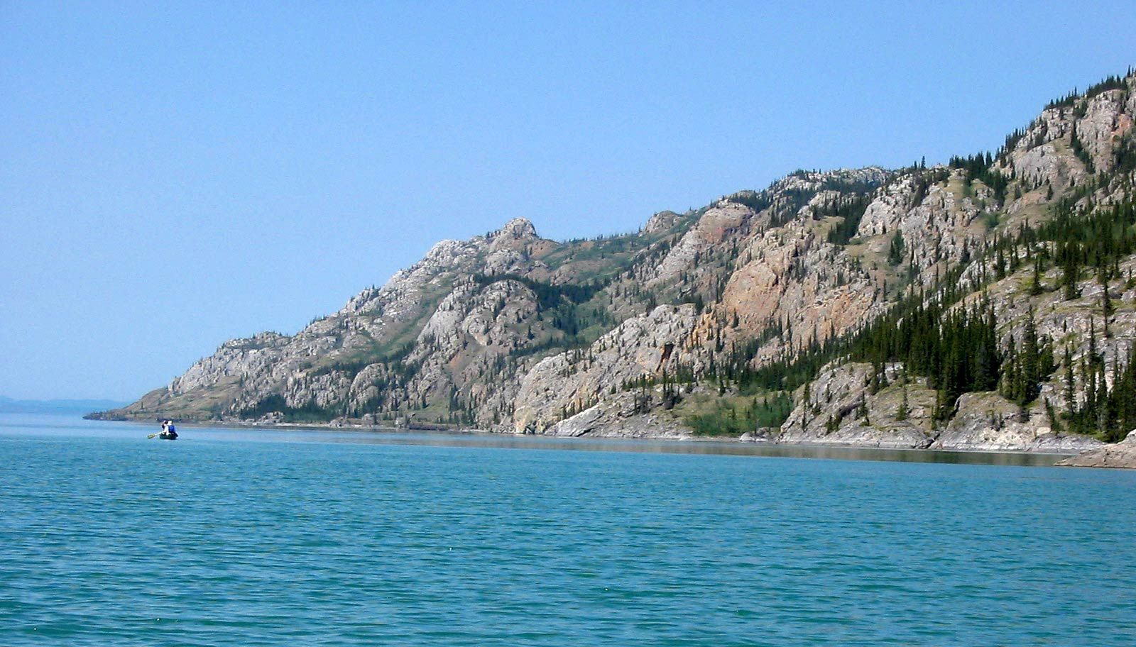 Rocky coastal cliffs beside calm blue sea under a clear sky, with a small boat in the distance