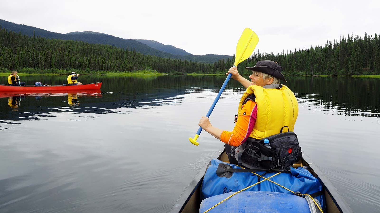 Kayaker in yellow life vest paddling on a calm lake beside forested mountains