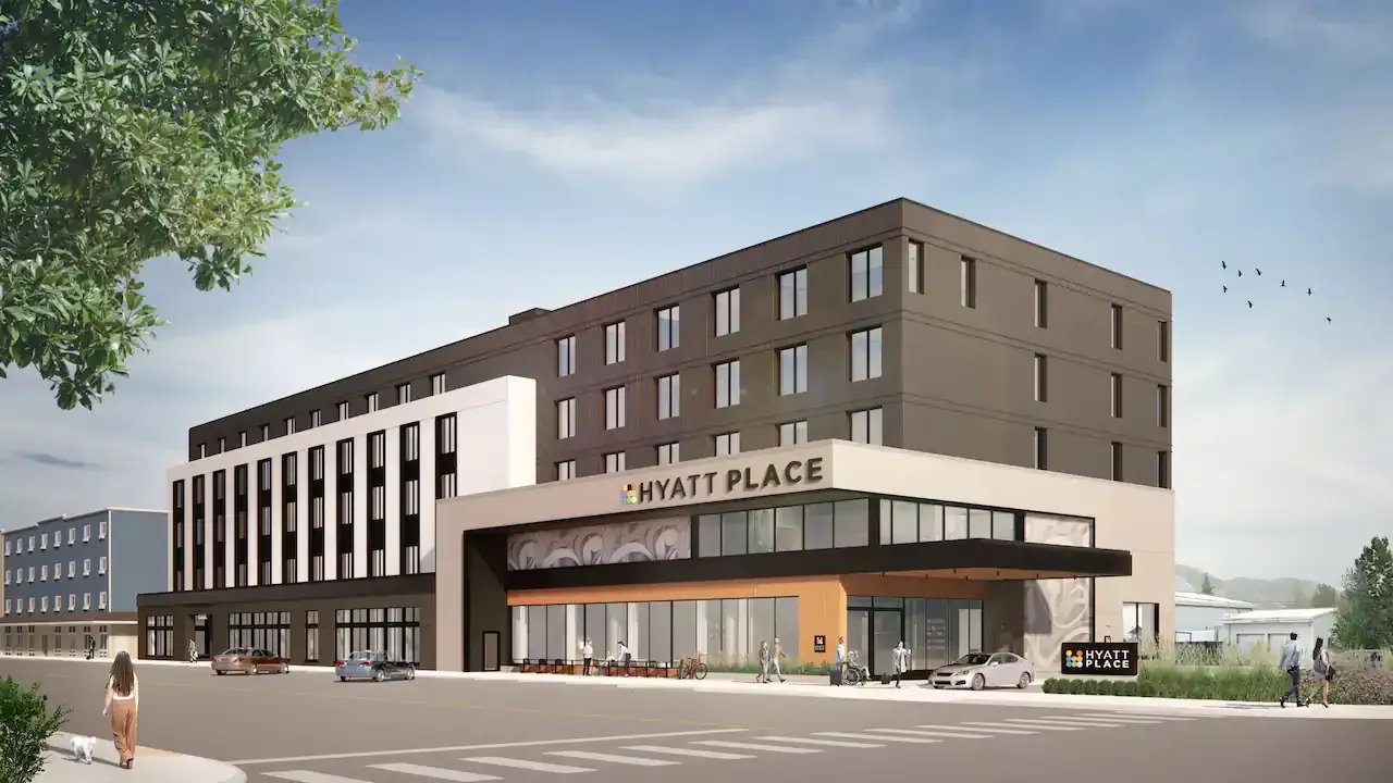 Modern hotel rendering with brown and white facade, street-level entrance, and trees at the corner.