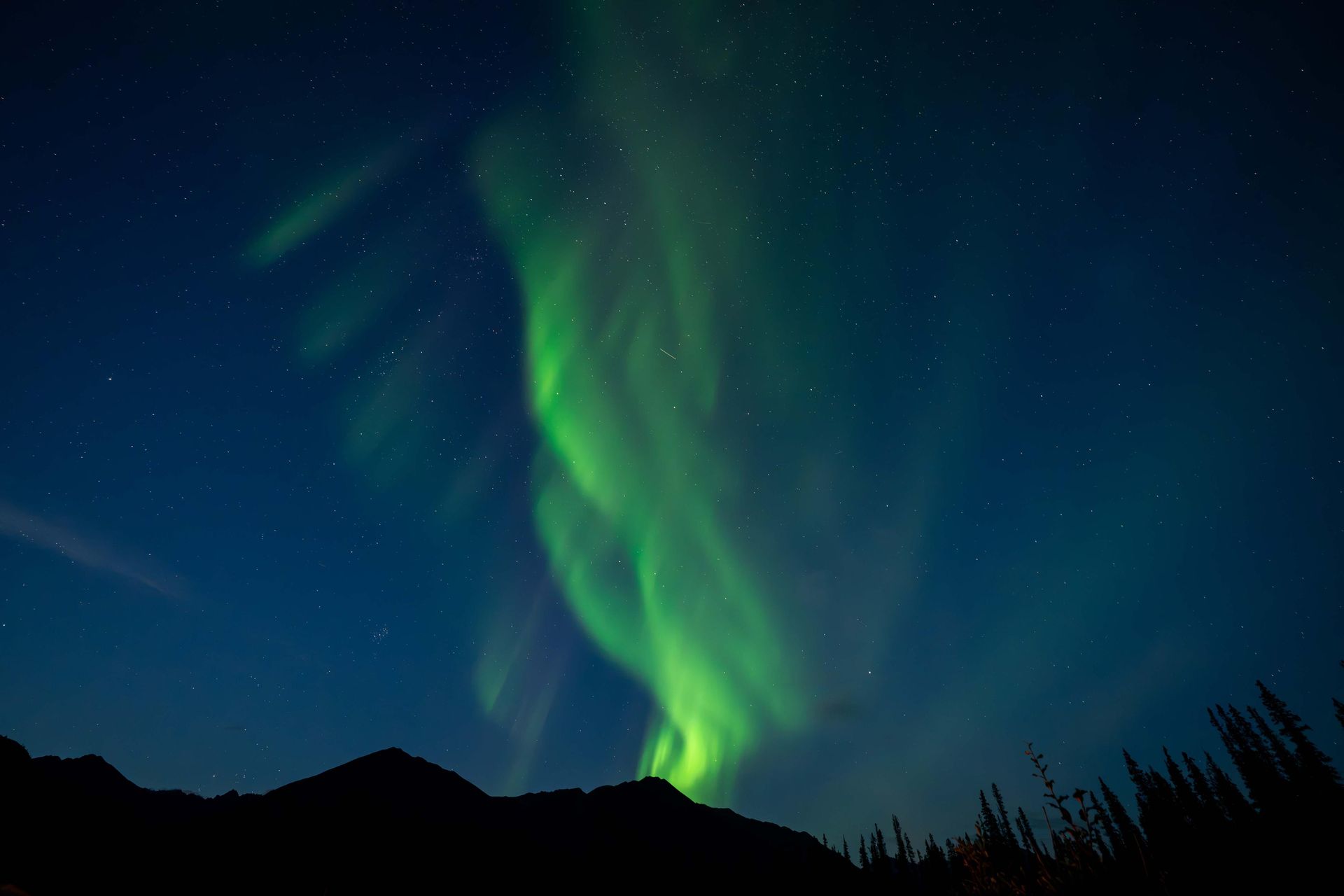 Green aurora swirling over dark mountain silhouettes in a night sky