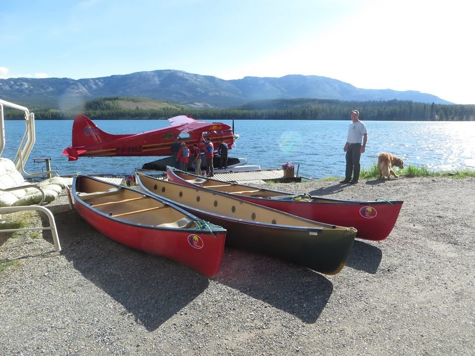 Three red canoes on a rocky lakeshore with a person standing by the water and mountains in the distance