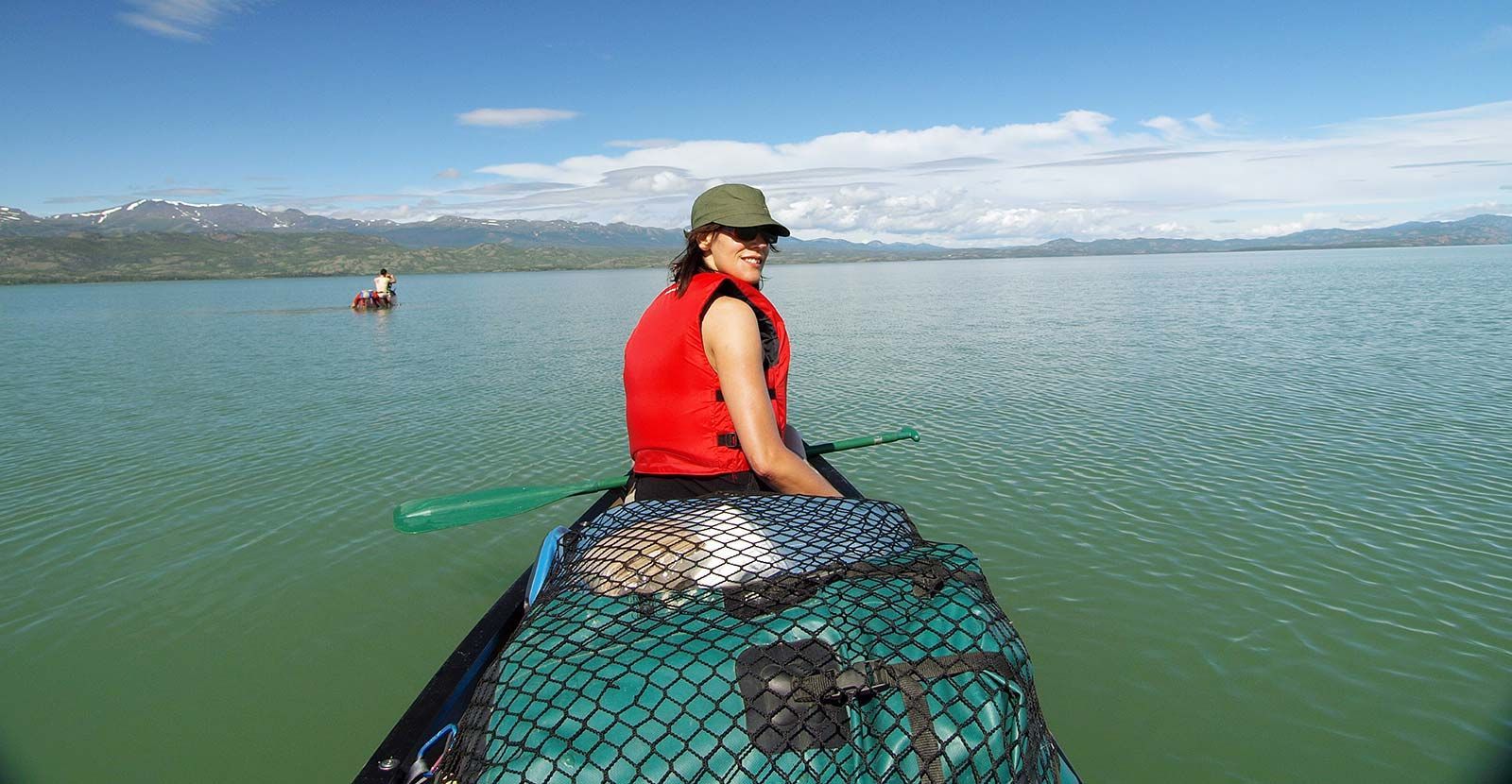 Person in a red life jacket sitting on a boat, looking over a calm lake with mountains in the distance