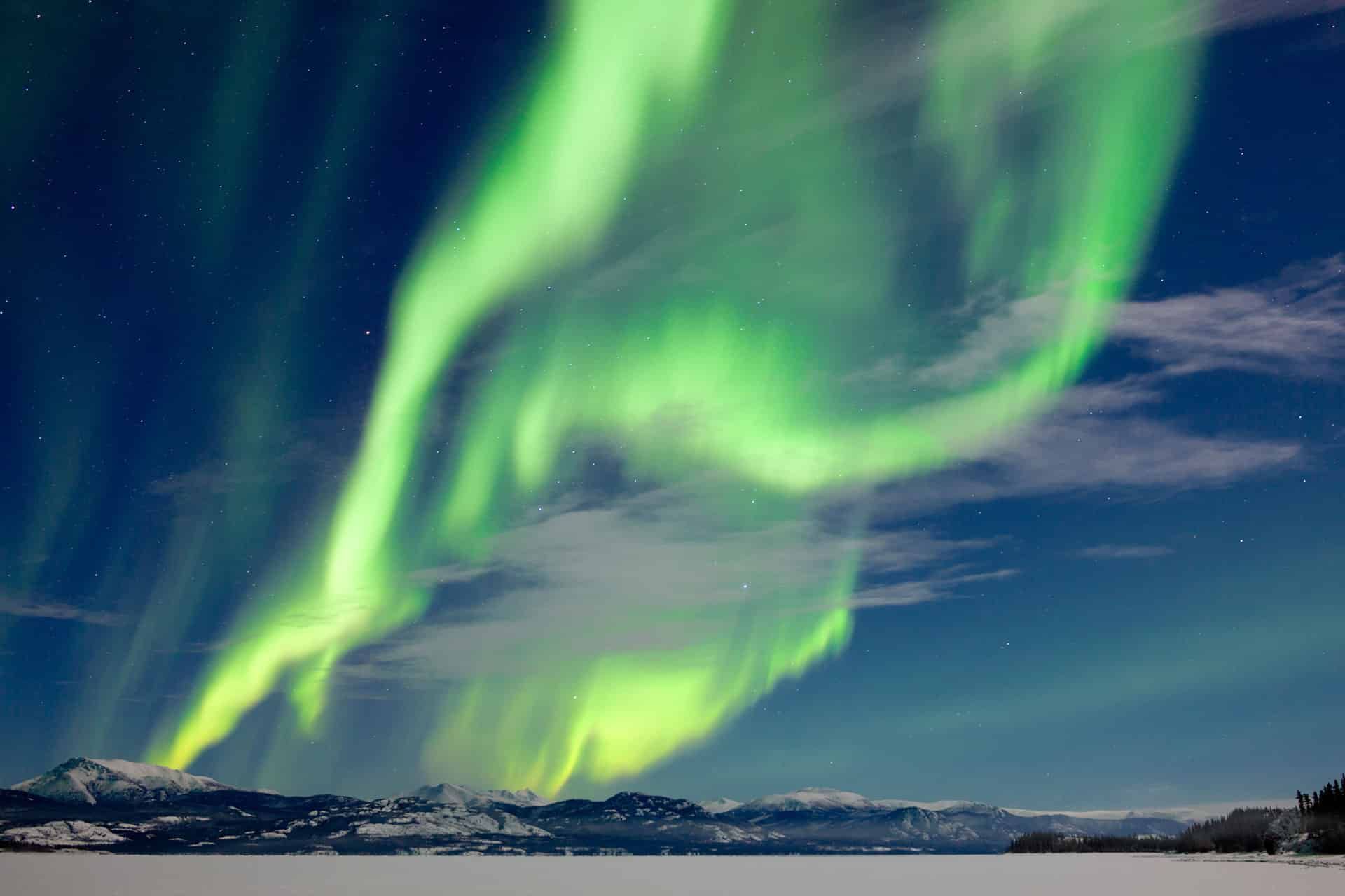 Green aurora borealis swirling over a dark snowy landscape and mountains at night