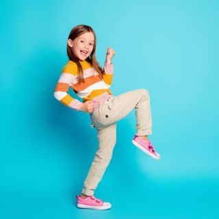 A little girl is standing on one leg on a blue background.