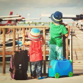 Two children are standing on a dock with their luggage.