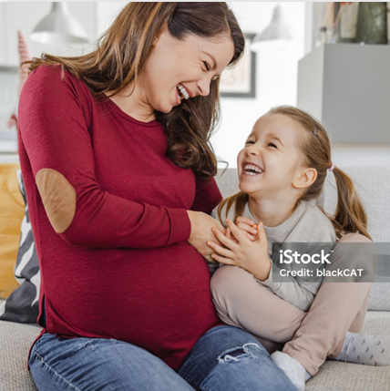 A pregnant woman is sitting on a couch with her daughter.