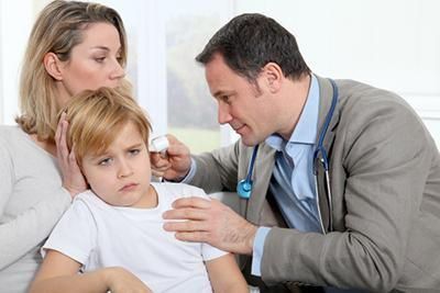 A doctor is examining a young boy 's ear while his mother looks on.