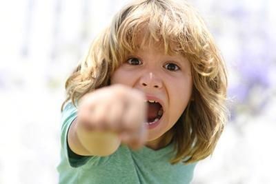 A young boy is pointing at the camera with his mouth open.