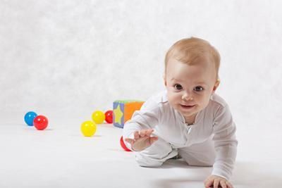 A baby is crawling on the floor with toys in the background.