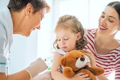 A little girl is holding a teddy bear and getting an injection from a doctor.
