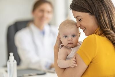 A woman is holding a baby in her arms in front of a doctor.