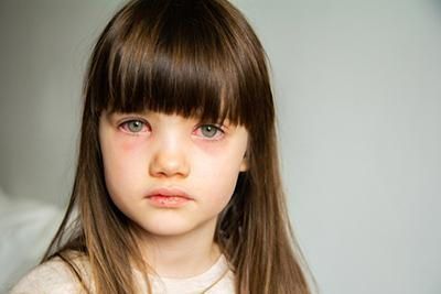 A little girl with long hair and bangs is crying and looking at the camera.