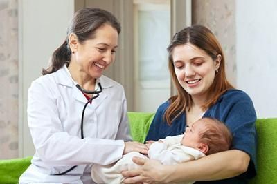 A woman is holding a baby while a doctor examines it.