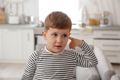 A young boy is sitting on a couch with his finger pointing to his ear.