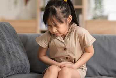 A little girl is sitting on a couch holding her stomach.
