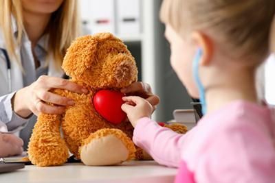 A little girl is examining a teddy bear with a stethoscope.