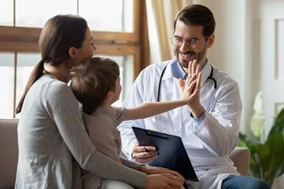 A doctor is giving a child a high five while sitting on a couch.