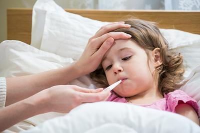 A little girl is laying in bed with a thermometer in her mouth.