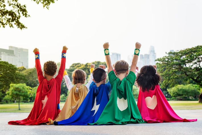 A group of children dressed in superhero costumes are standing next to each other with their arms in the air.