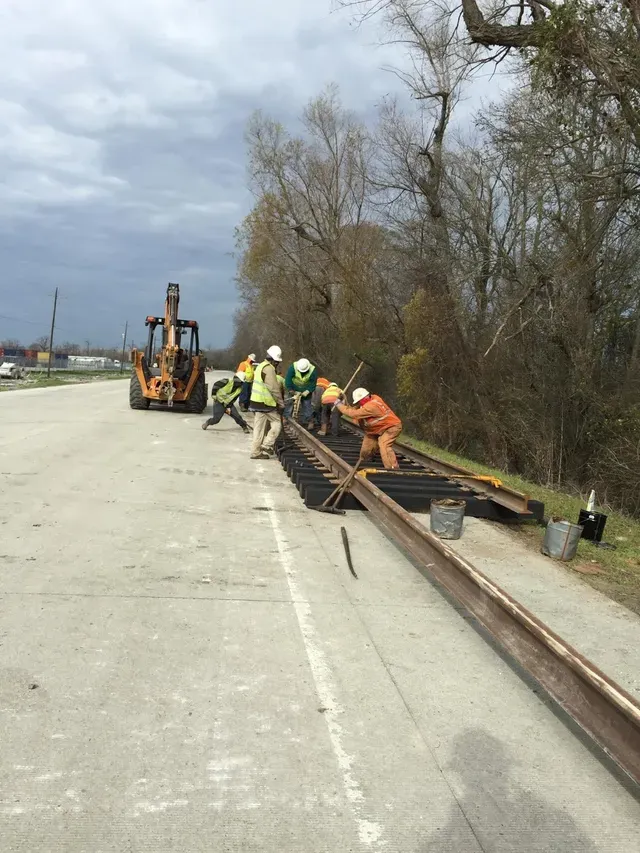 A group of construction workers are working on train tracks on the side of a road.