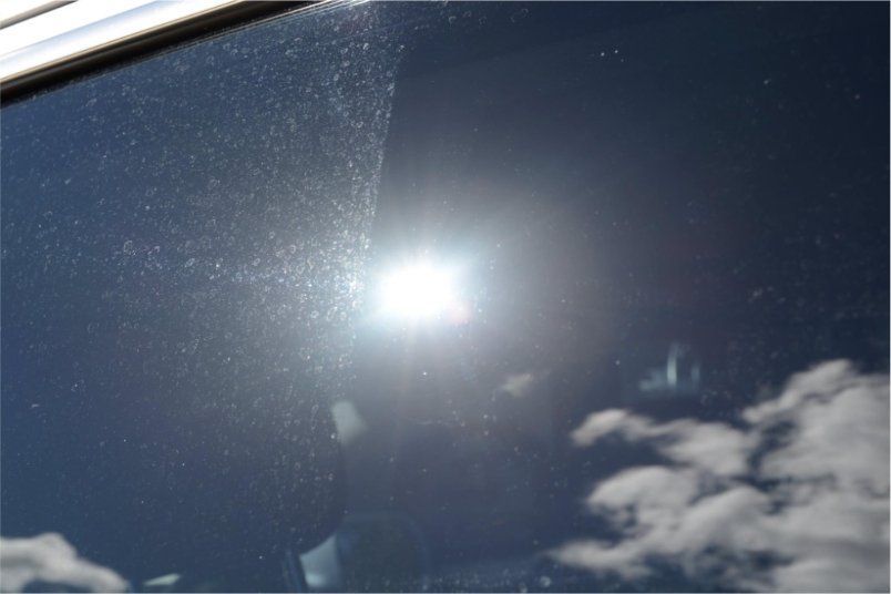 Sun shining through a partially cleaned window, showing streaks and dirt. Sky and clouds reflected.