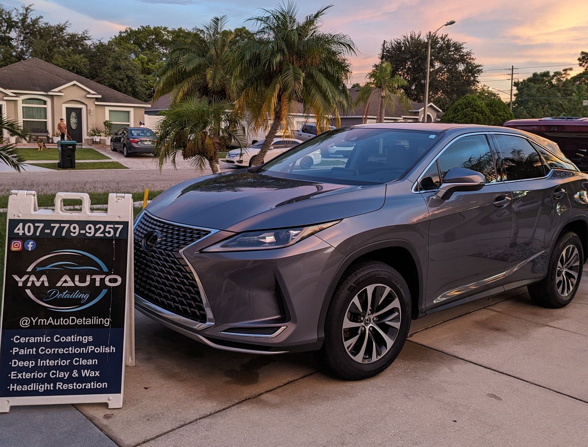 Gray Lexus SUV parked in front of a sign for YM Auto Detailing.