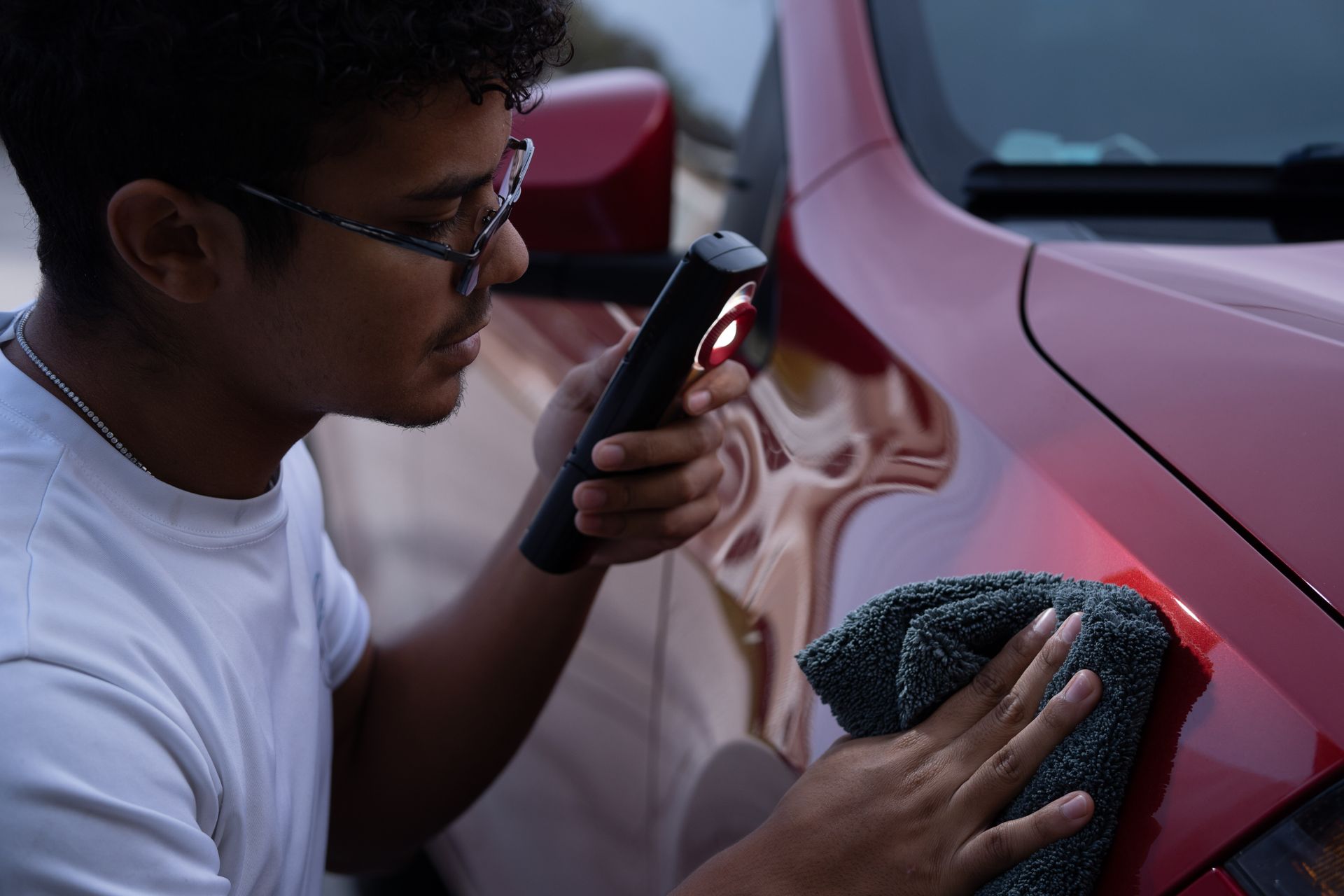 Man inspecting red car paint with a flashlight and a microfiber cloth.