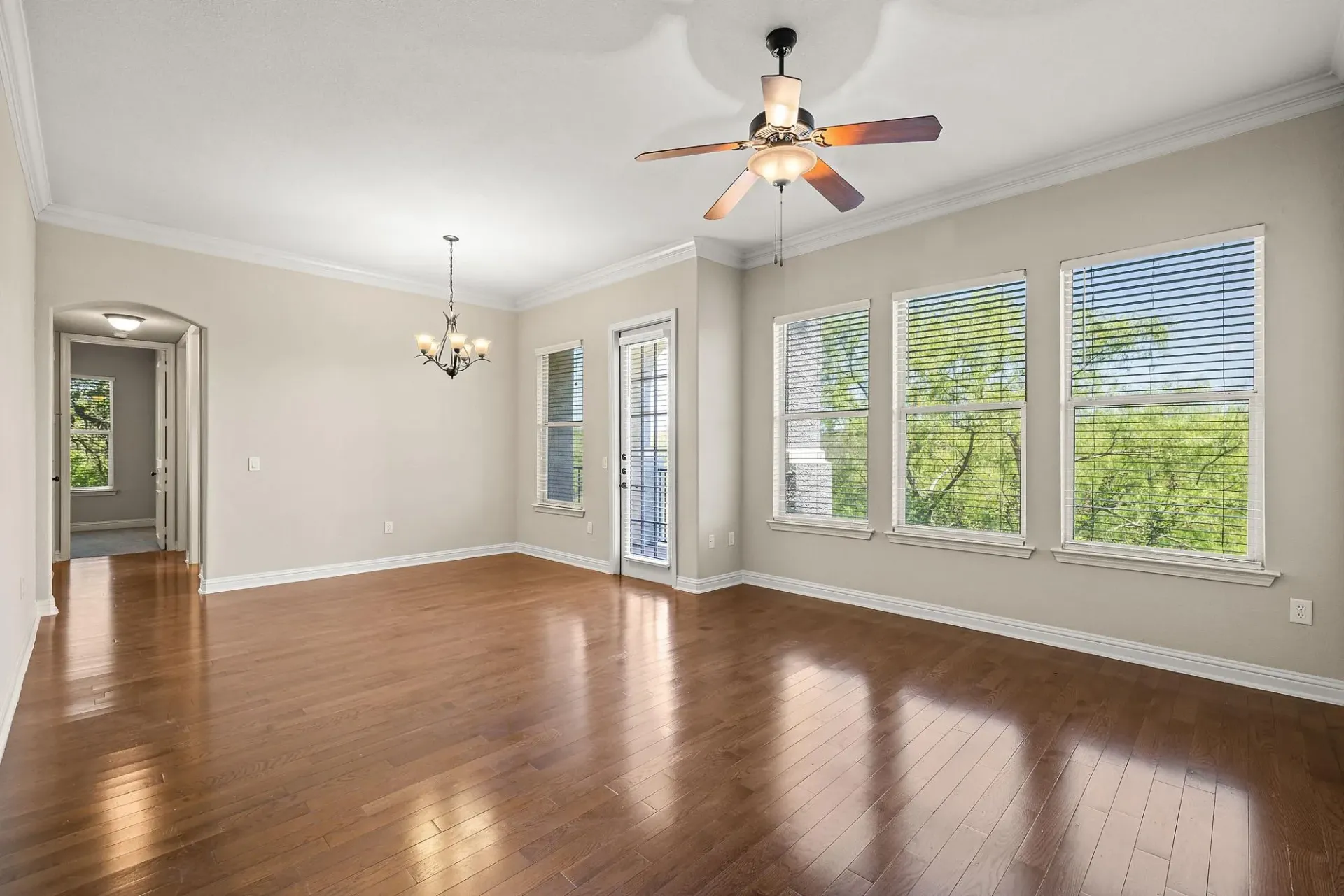 Spacious living area with hardwood floors, a ceiling fan, and large windows overlooking trees.