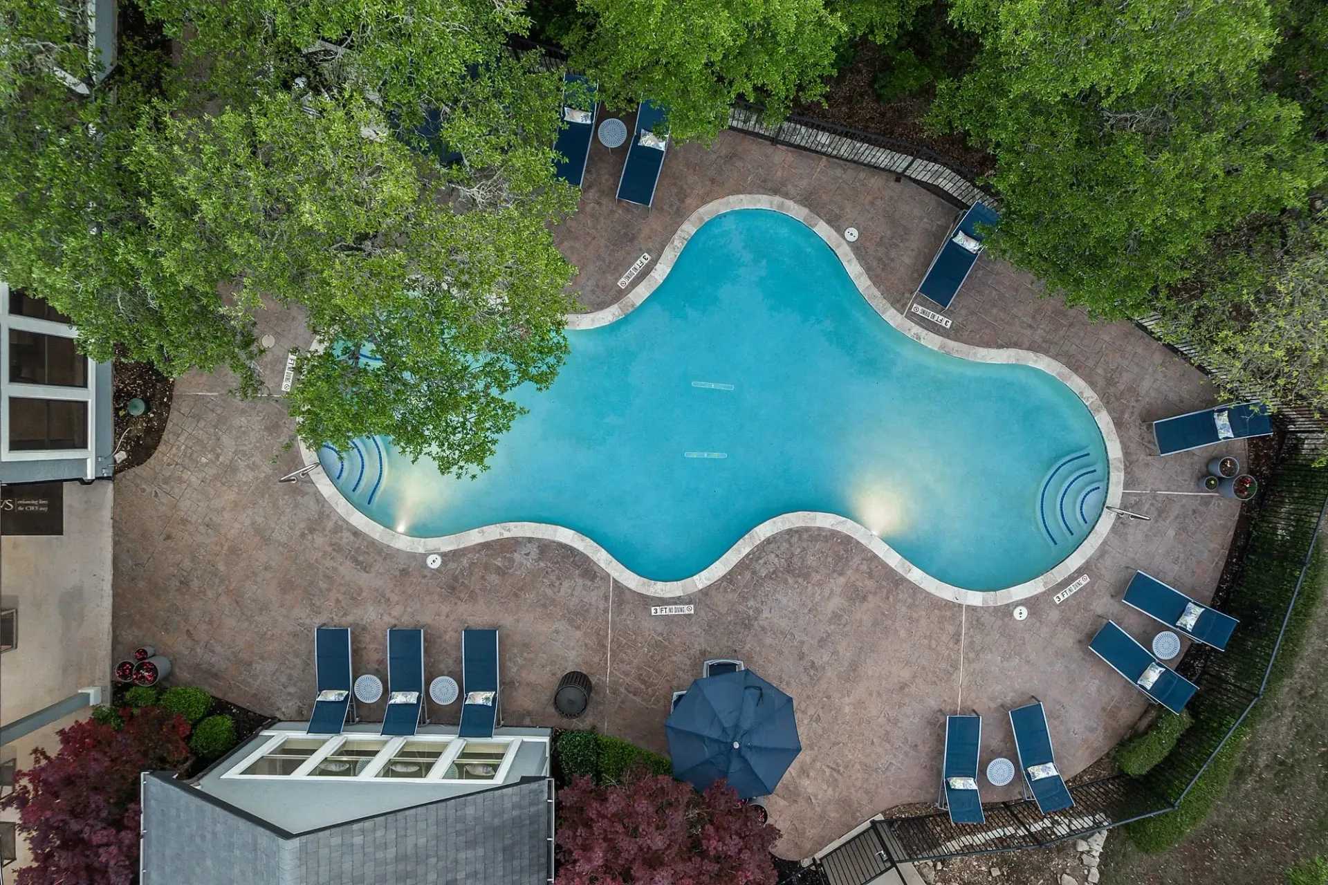Aerial view of a resort-style swimming pool with lounge chairs and umbrellas.