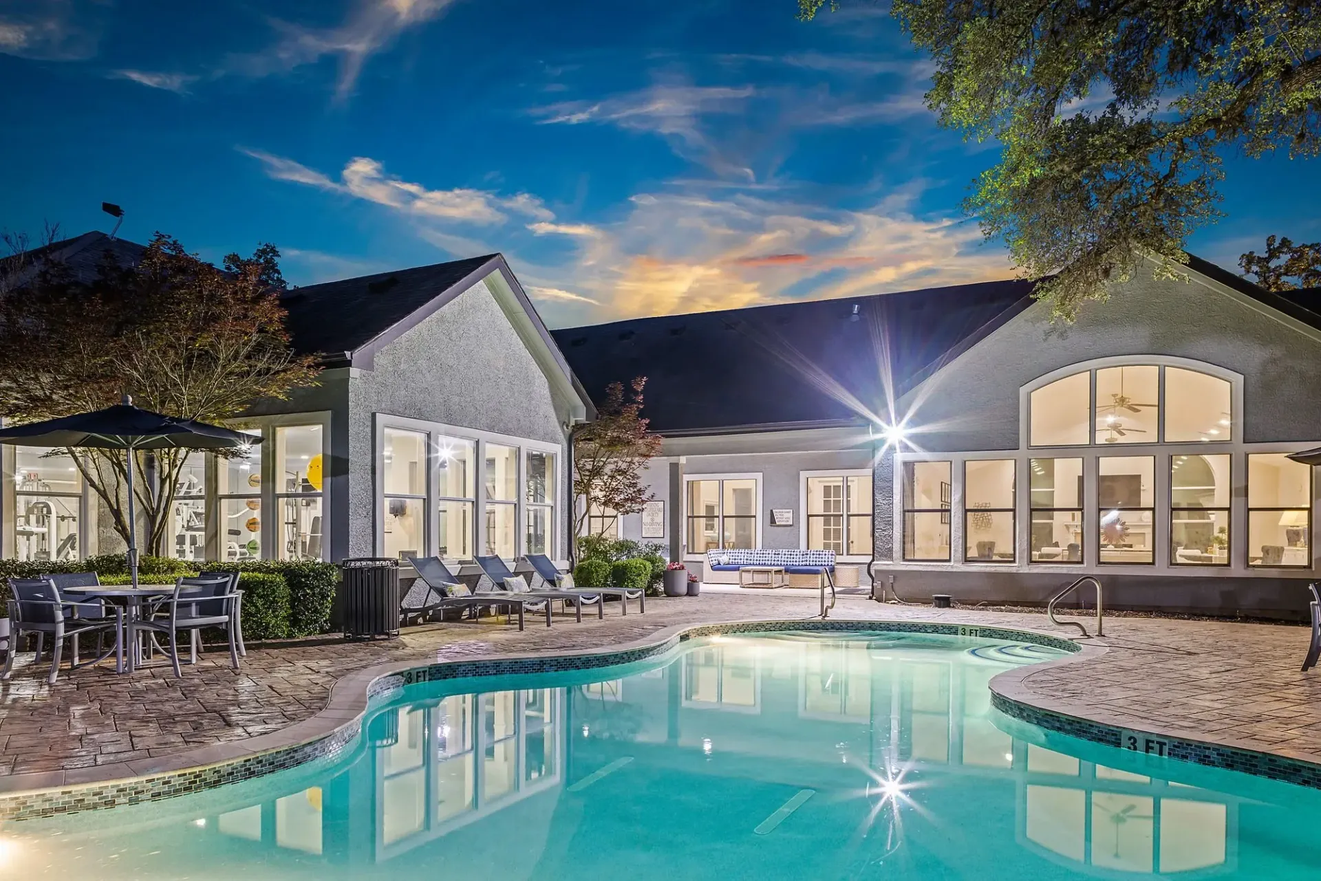 Resort-style swimming pool and lounge area at dusk with building lights on.