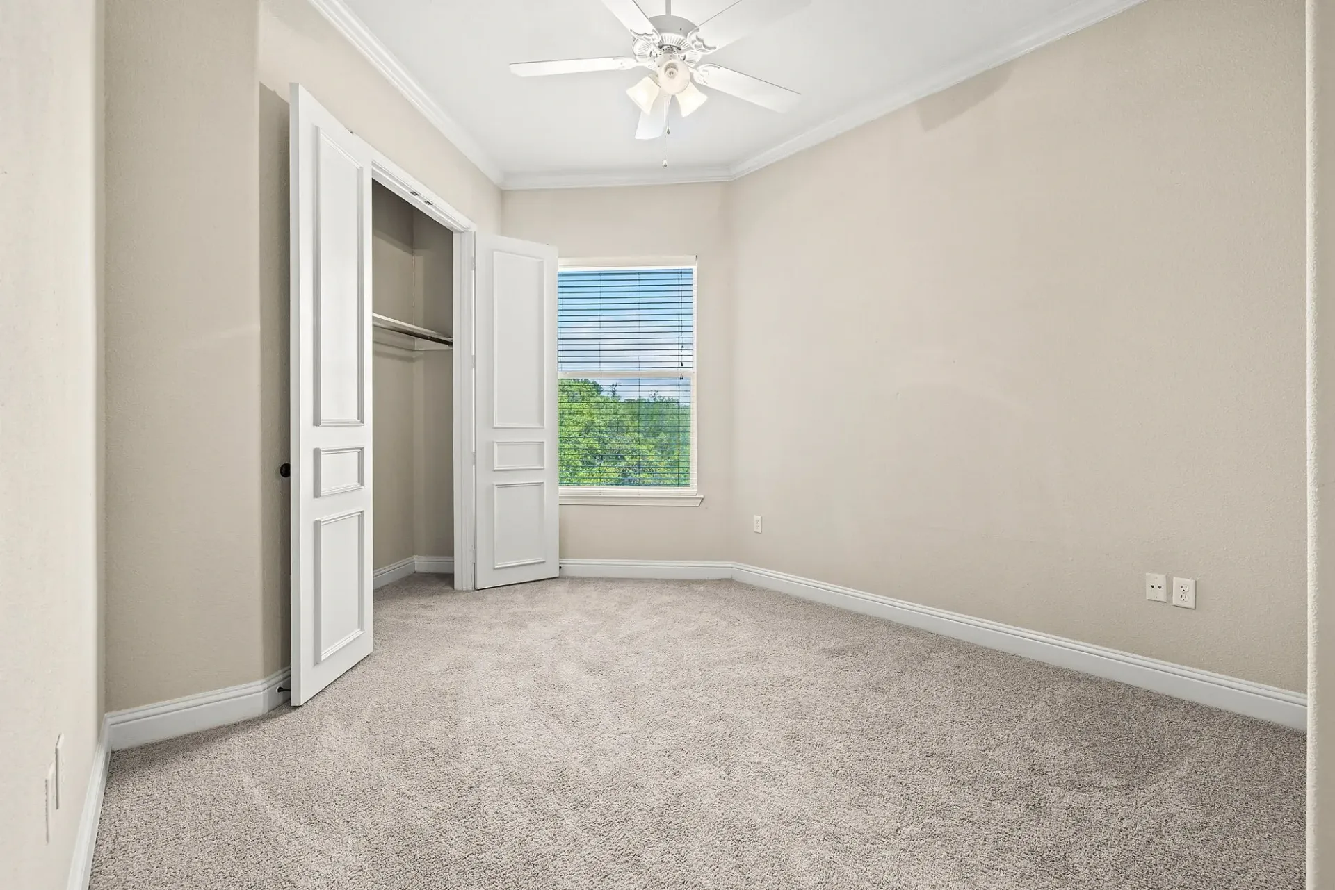Empty bedroom with white doors open to a closet, a ceiling fan, and a window with blinds.