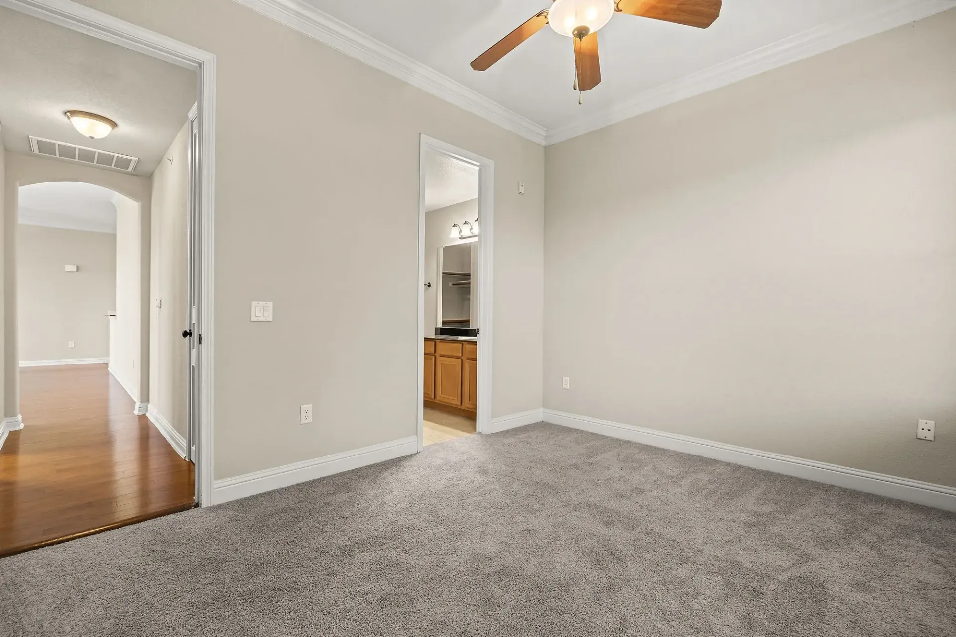 Bedroom with carpet and a ceiling fan, opening to a hallway and bathroom.