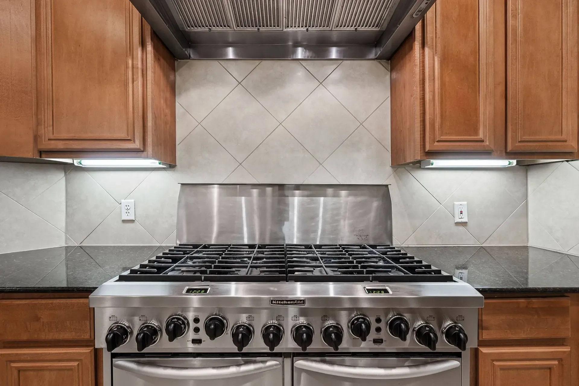 Stainless steel gas range with dark granite countertops and wood cabinetry.