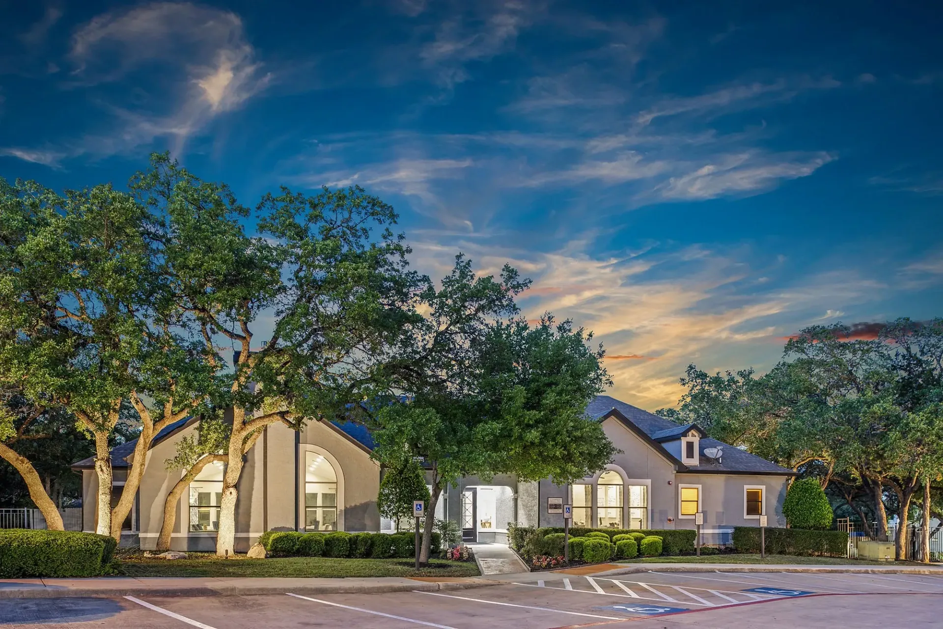 Exterior of multifamily property building with large trees and dramatic sunset sky.