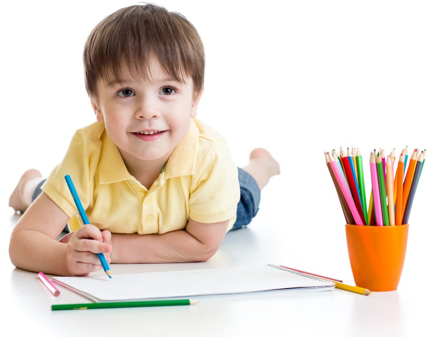 Young child lying on the floor drawing with a blue pencil; colored pencils are in an orange cup beside the paper.
