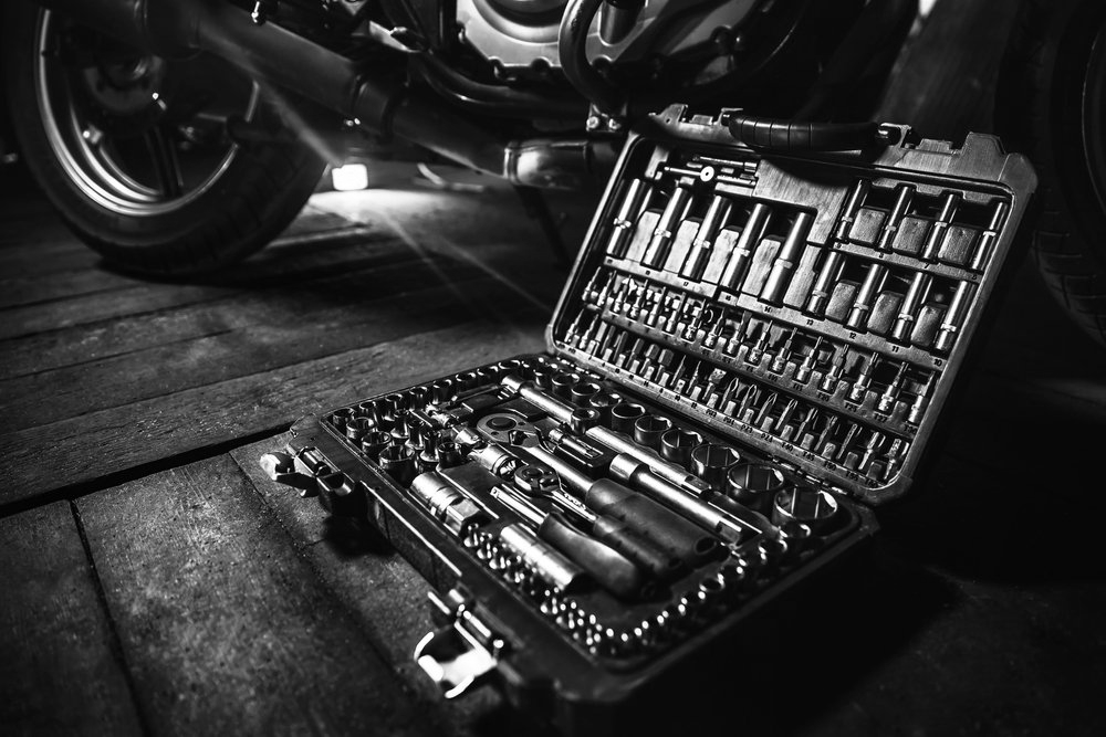 Open toolbox with tools, and motorcycle wheel in the background, in black and white.