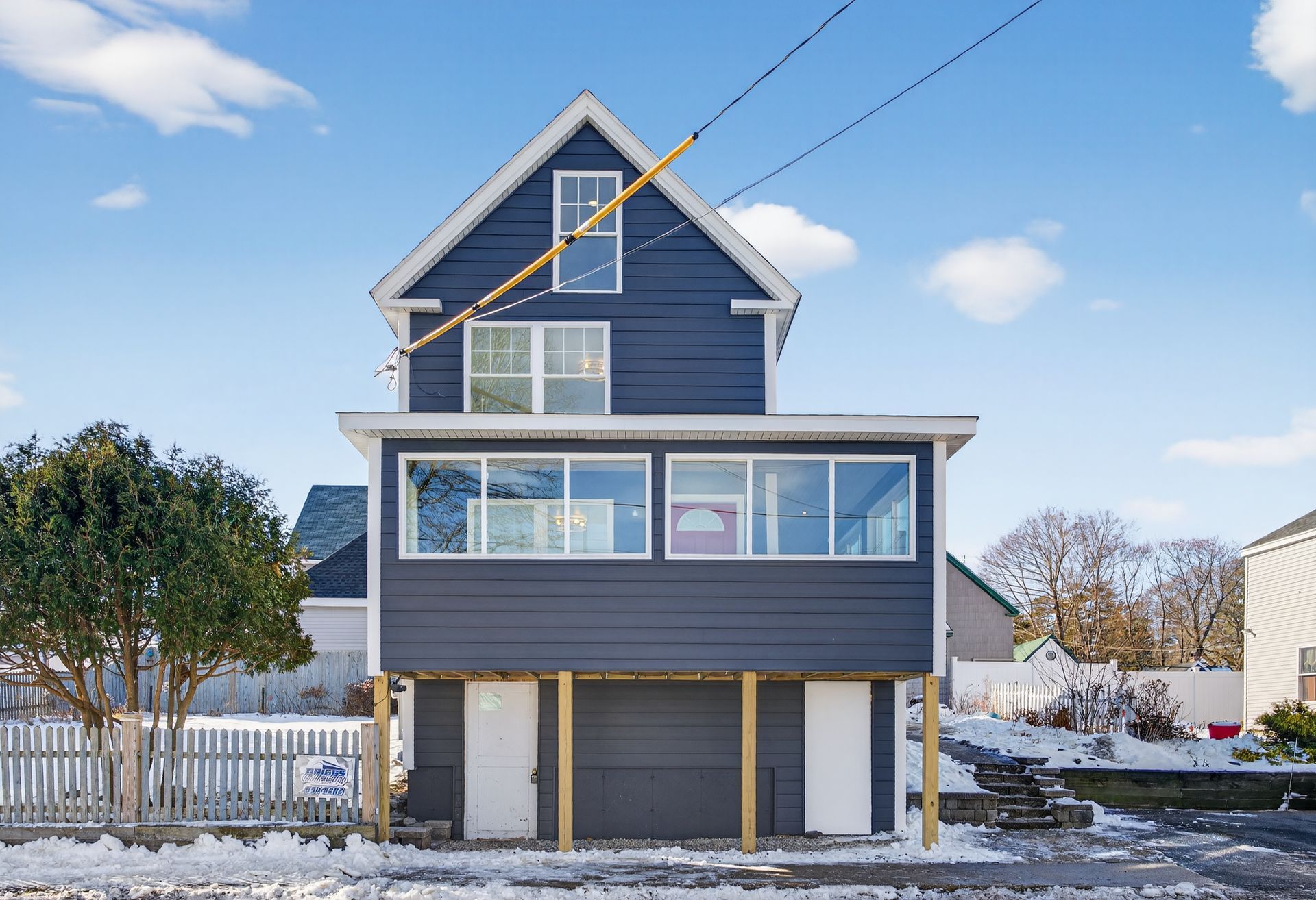 Two-story blue house on a snowy street with white doors and large windows.