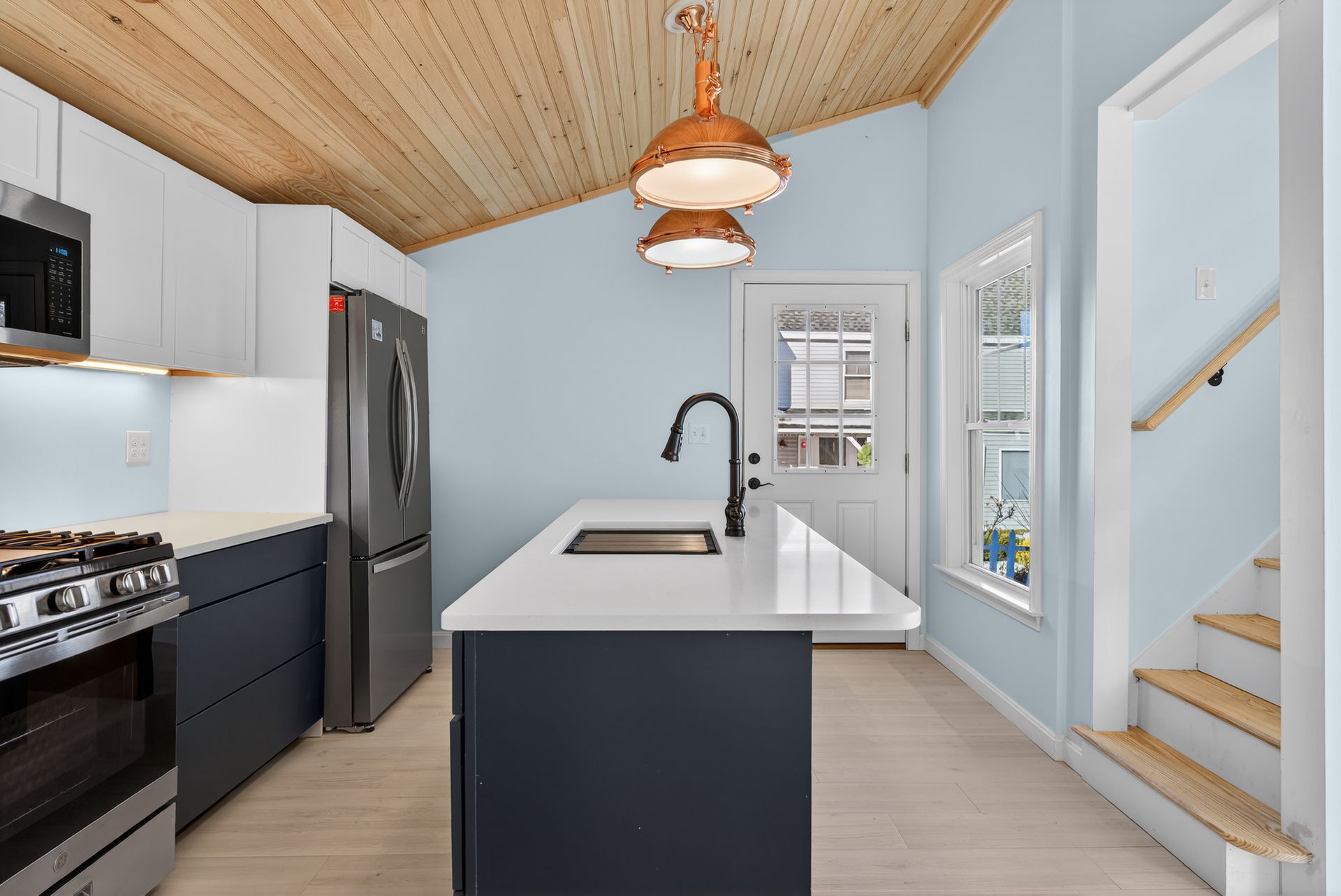 Modern kitchen with wood ceiling, blue walls, island, and stainless steel appliances.