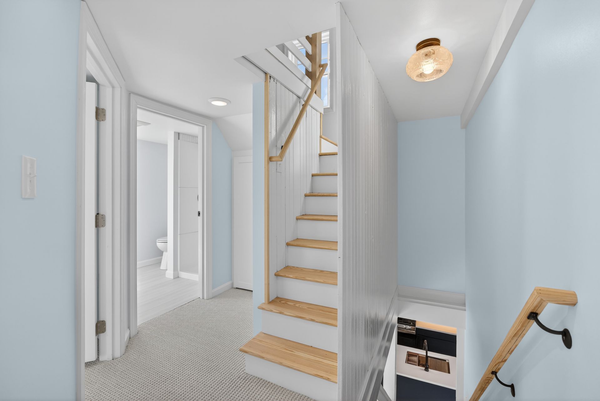 Staircase in a light blue hallway with a bathroom visible down a hallway.
