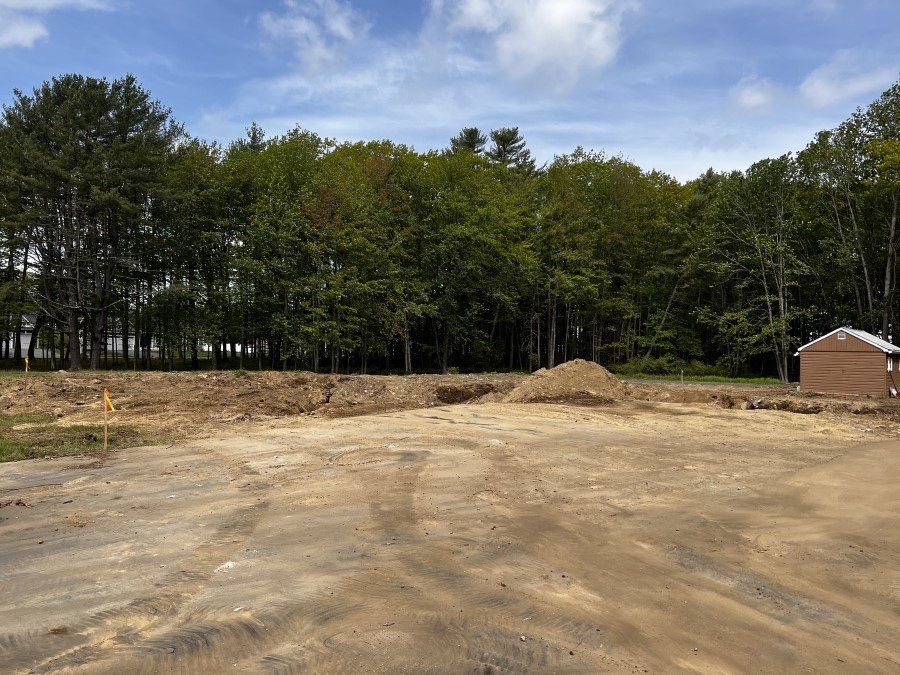 Cleared dirt lot with trees in the background, blue sky, and a small shed on the right