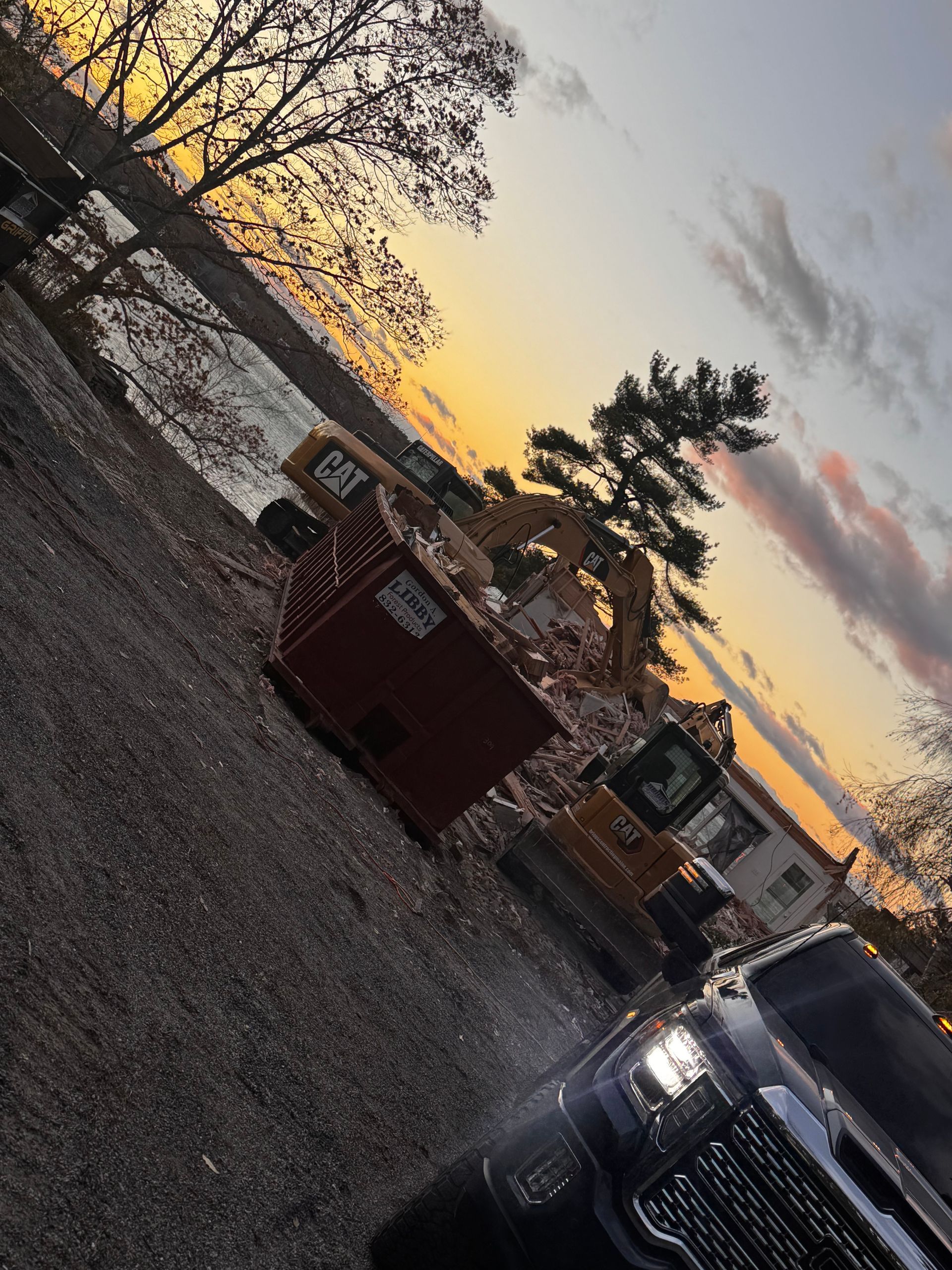 Construction equipment at sunset by a body of water.