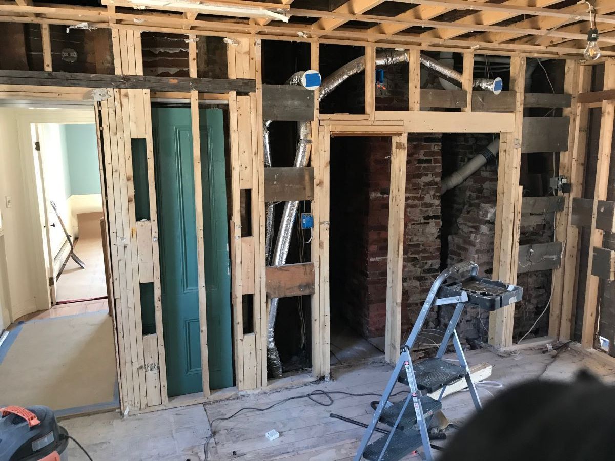 Interior of a house under renovation with exposed framing, drywall, and a ladder on the floor.